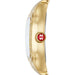 A close-up side view of a gold-tone watch with a white dial and a red circular crown accent featuring a white 'MW' logo.