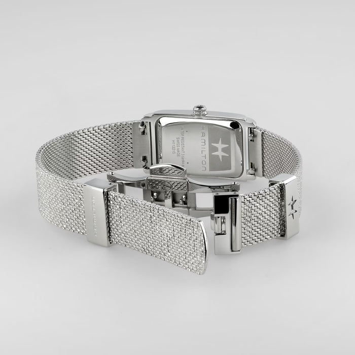 Silver-tone stainless steel watch with a mesh band, shown from the back on a light gray background. The brand name 'AMICOR' is engraved on the watch case.