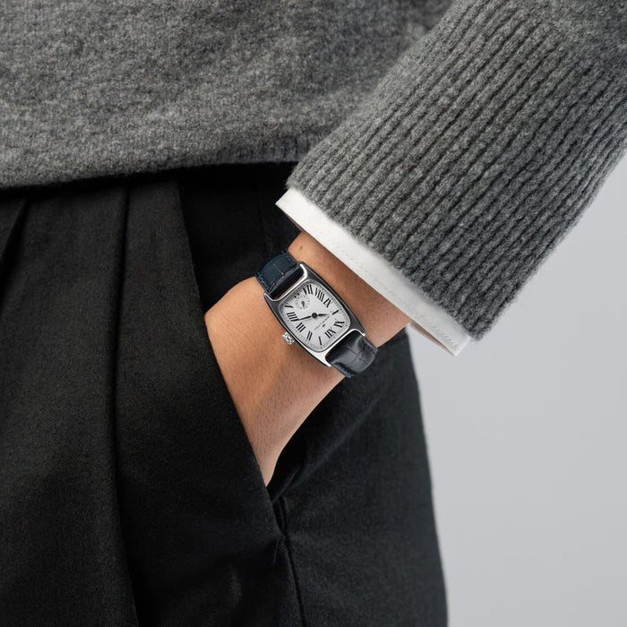 Person wearing a black wristwatch with a gray sweater and black coat on a neutral background