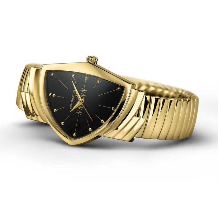 A gold-tone watch with a shield-shaped case, a textured link bracelet, and a black dial with gold hands and markers, shown on a clean white background.