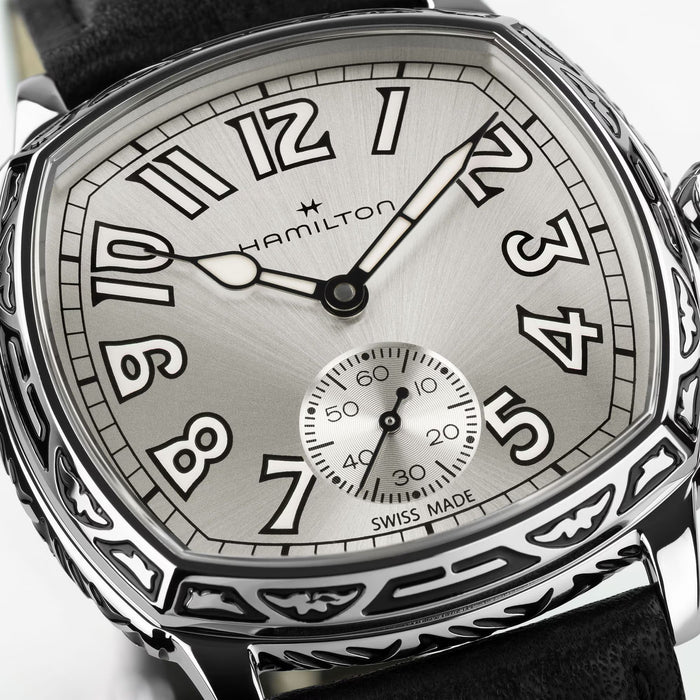 Hamilton watch with a silver sunburst dial, black Arabic numerals, a small seconds subdial, and an engraved silver-tone case on a black leather strap.
