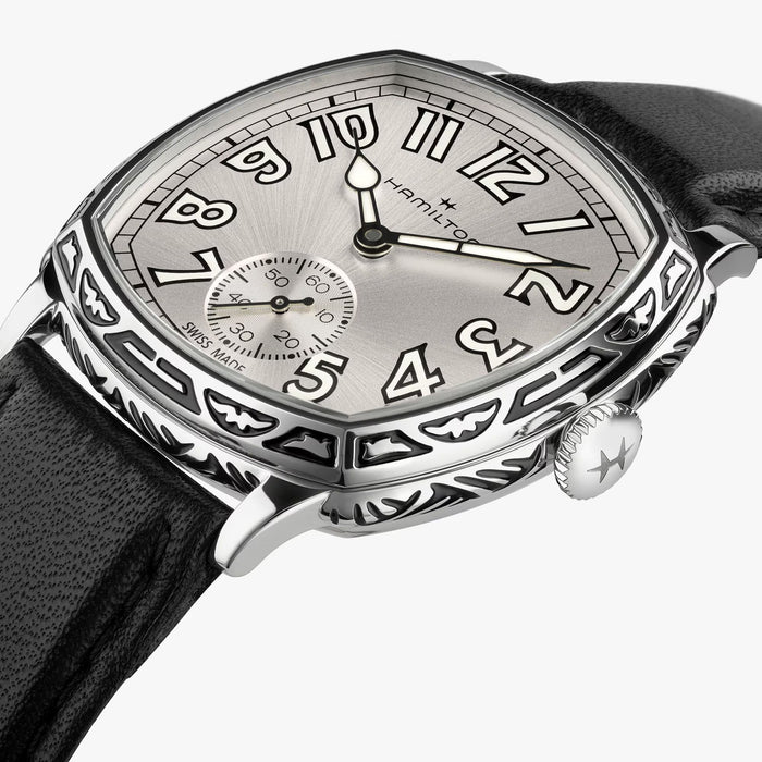 A close-up of a Hamilton watch with an octagonal silver dial, black leather strap, and a highly polished silver case featuring intricate hand-engraved details and bat-wing motifs.