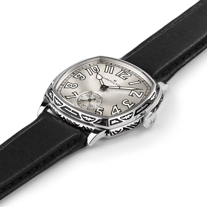 A close-up of a Cartier watch with a silver-toned shield-shaped dial, black Arabic numerals, and a black leather strap on a white background.
