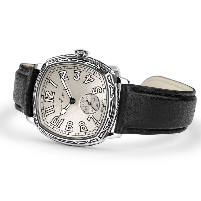 A luxury watch by Richard Mille, featuring a silver-toned bezel with intricate cutouts, a silver dial with black Arabic numerals, and a black leather strap, shown on a white background.