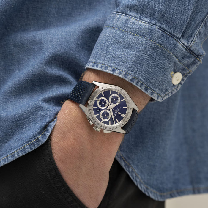Close-up of a wrist wearing a watch with a blue face, set against a denim background.