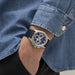 Close-up of a wrist wearing a watch with a blue face, set against a denim background.