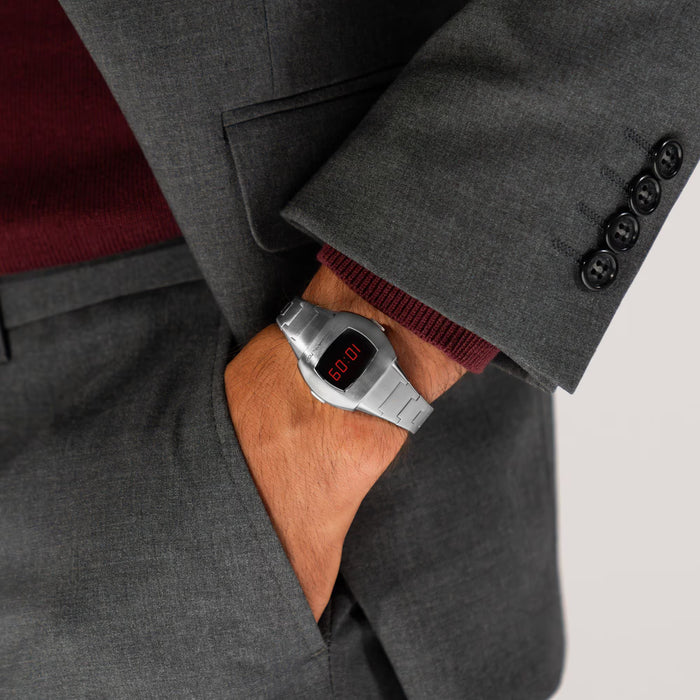 Person wearing a gray suit with a digital wristwatch on a neutral background