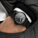 Black wristwatch on a person's wrist with a blurred background