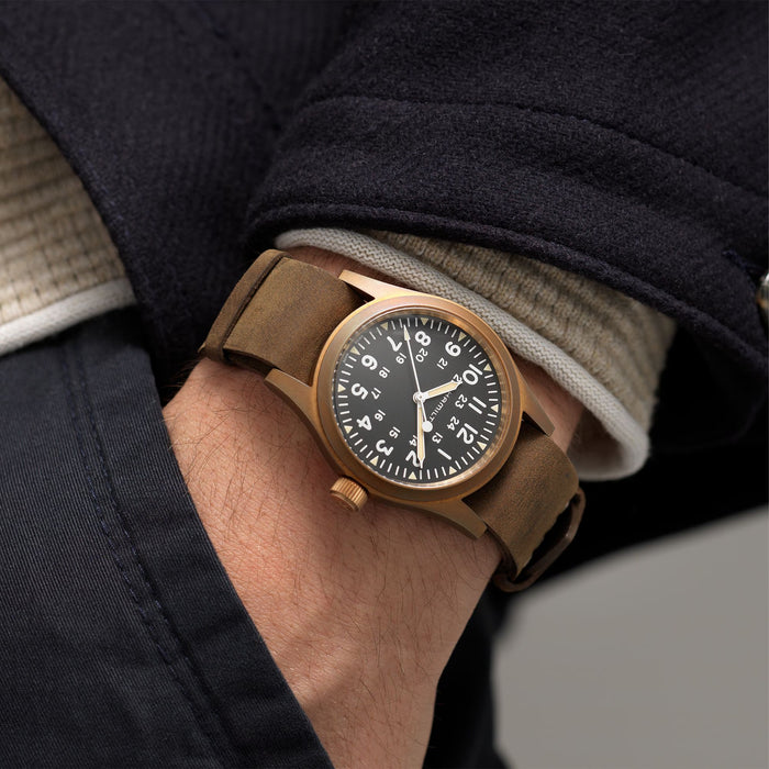Close-up of a wrist wearing a bronze watch with a dark face, against a neutral background.