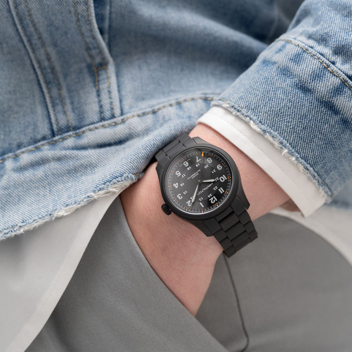 Person wearing a black wristwatch with a denim jacket and gray pants.