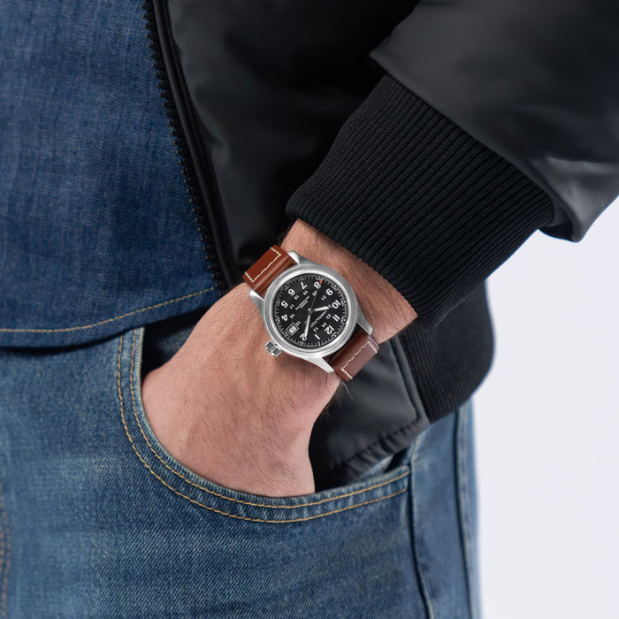 Person wearing a watch with a brown leather strap on a plain background