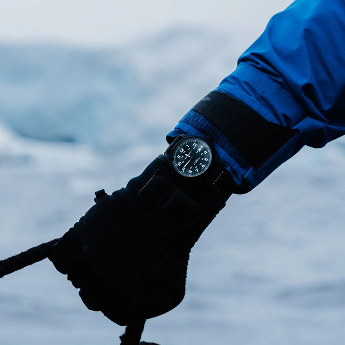 Hand wearing a black glove and watch, holding onto a rope with water in the background