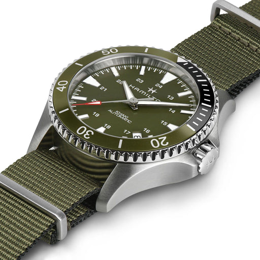 Hamilton watch with an olive green dial and matching green nylon strap, featuring a silver stainless steel case and a black rotating bezel.