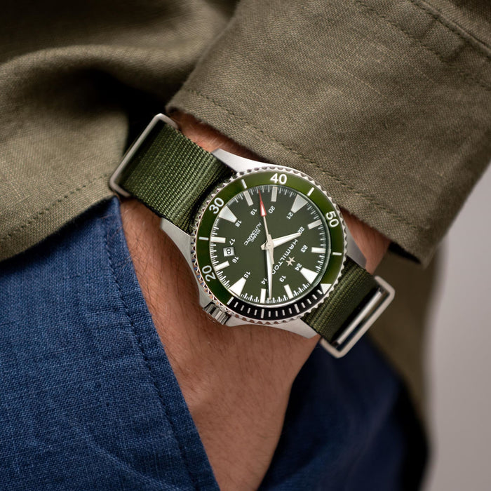 Green watch with a green strap on a person's wrist, wearing a green jacket and blue pants.