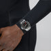 Close-up of a wrist wearing a silver watch with a black strap against a neutral background