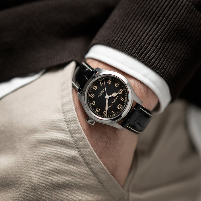 Close-up of a person wearing a black wristwatch with a brown leather strap.