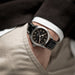 Close-up of a person wearing a black wristwatch with a brown leather strap.
